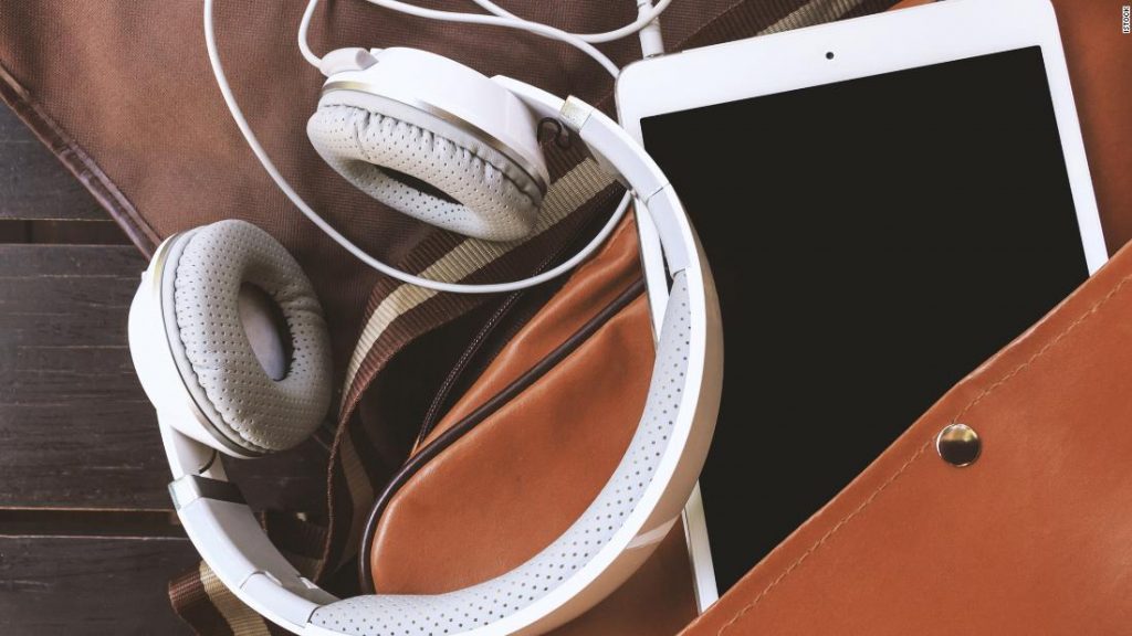 Overhead view of an open messenger bag lying flat with a tablet and headphones set on top